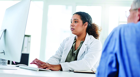 African American female laboratorian in a white coat sitting at a desk with a patient
