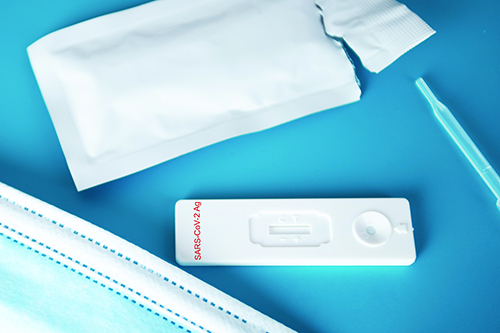 A SARS-CoV-2-Ag antigen test placed in between a blue mask and the test packaging.