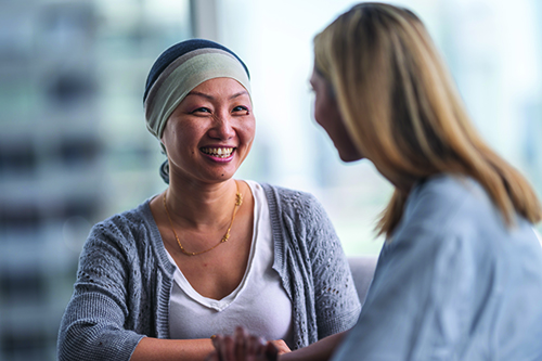 An Asian woman sitting at a table and smiling at a woman healthcare professional sitting next to her