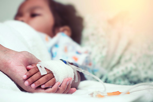 A child in a hopstial bed holding an adults hand.