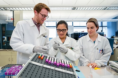A male and 2 women laboratorians labeling blood samples in a lab.