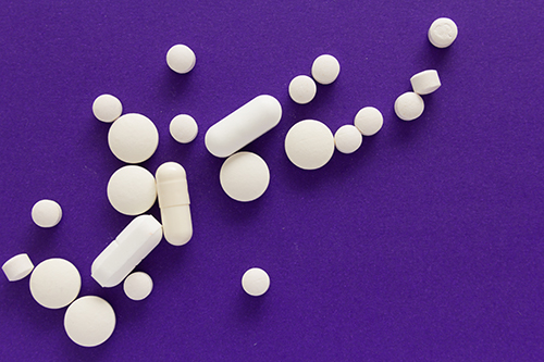 An assortment of white pills in front of a purple background.