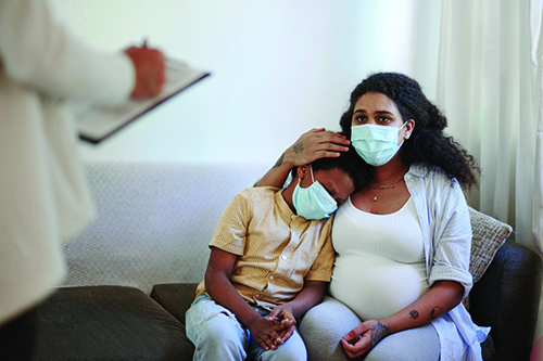 A woman in a mask sitting on a couch holding her son.