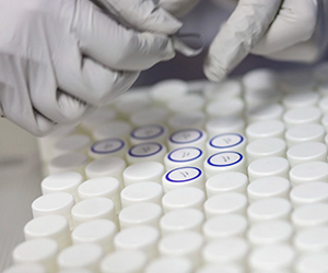 two hands in white gloves labeling testing tubes