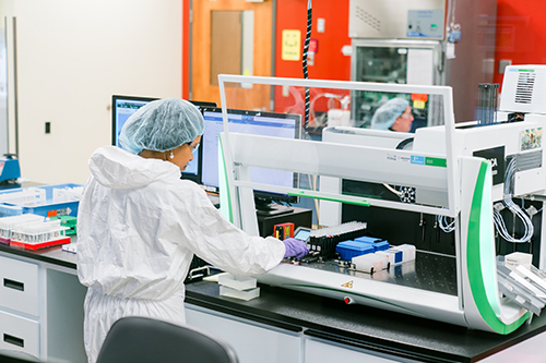Female laboratorian in a lab coat and hair cover working on patient samples.