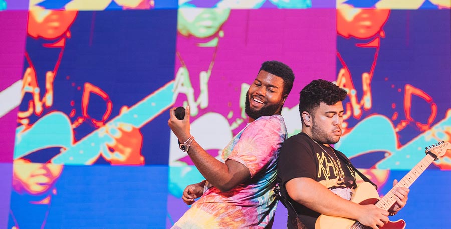 Colorful photo of Khalid and guitarist on stage rocking out