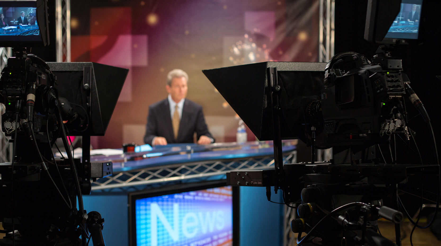 news anchor at anchor desk as seen from behind camera