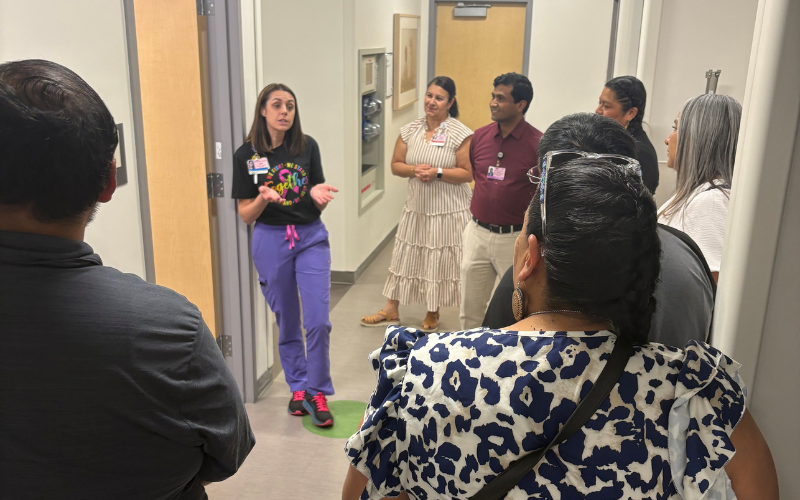 A person in scrubs is speaking to a group of people in a hallway.