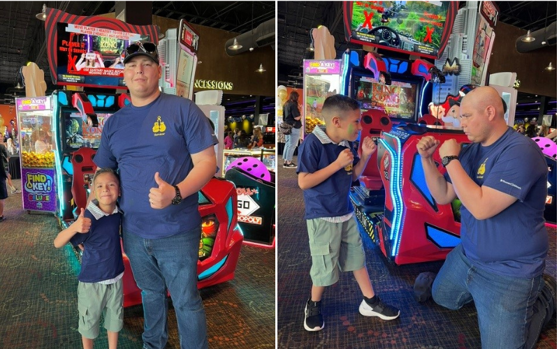 A man and a child stand in front of arcade games, both giving a thumbs up.