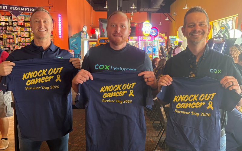 Three men hold up navy blue t-shirts with yellow lettering that reads 
