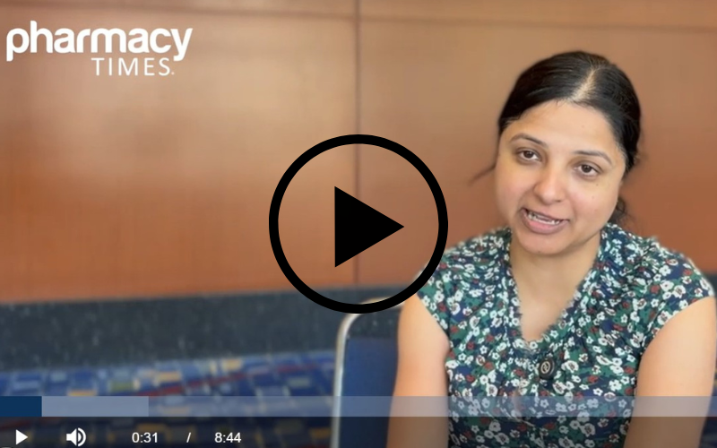 A woman, Parichita Choudhury, MD, in a floral shirt speaks in front of a wall with the Pharmacy Times logo.