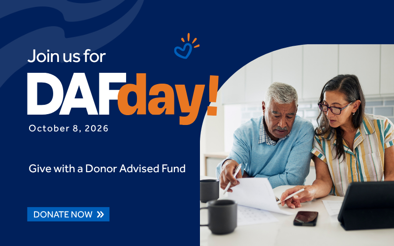 Promotional banner for DAy of Giving on October 8, 2026, with text “Join us for DAy of DAy” and “Give with a Donor Advised Fund,” plus “Donate Now,” beside a photo of two people reviewing documents at a table.