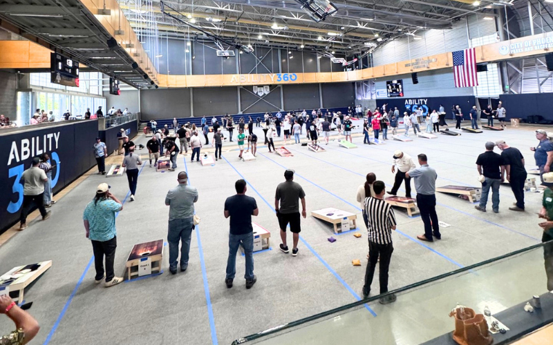 A large indoor event with many people playing a game of cornhole with multiple boards set up and marked lanes.