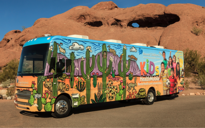 A colorful bus decorated with desert animals and cacti, branded as 