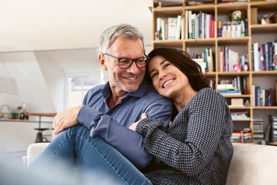 Mann und Frau sitzen auf einem Sofa, umarmen sich und lächeln