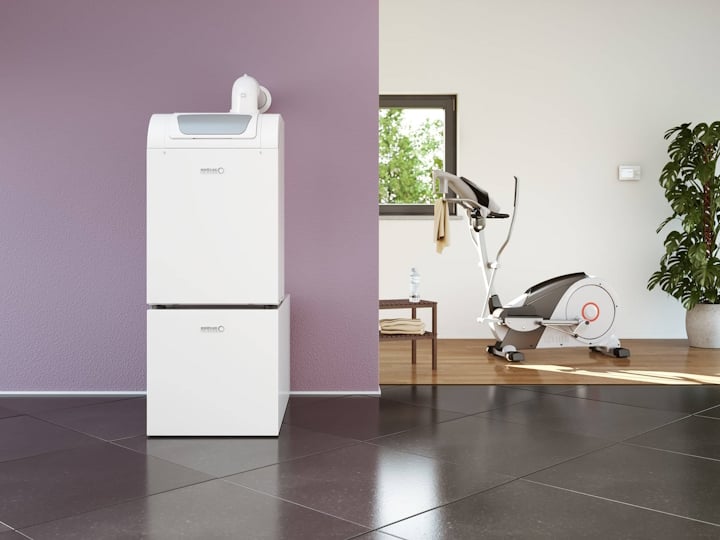 Der Gas-Brennwertkessel BGB EVO von Brötje steht vor einer fliederfarbenen Wand, im Hintergrund ein Hometrainer, Fenster und eine große Zimmerpflanze.