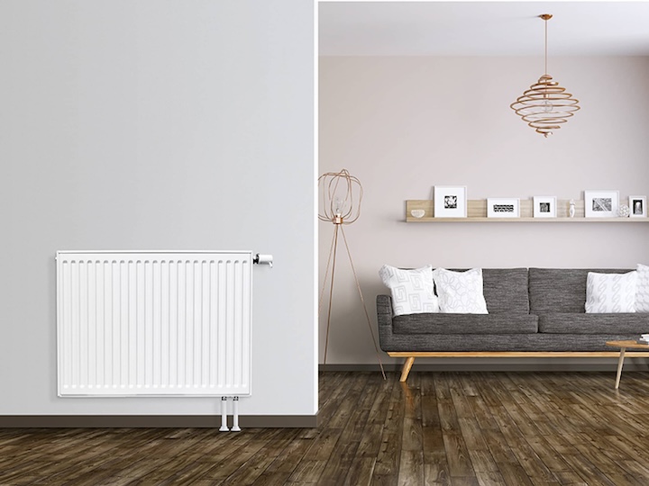 Ein EuroProfil-Flachheizkörper an einer hellgrauen Wand, rechts ein Wohnzimmer mit einer Couch.