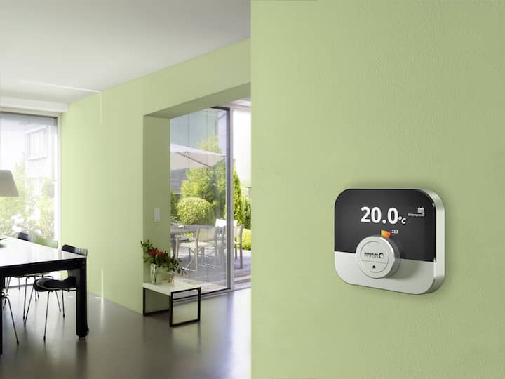 Die Regelung des Raumgerätes ISR IDA an einer grünen Wand im Wohnraum eines Hauses mit Blick in den Garten.