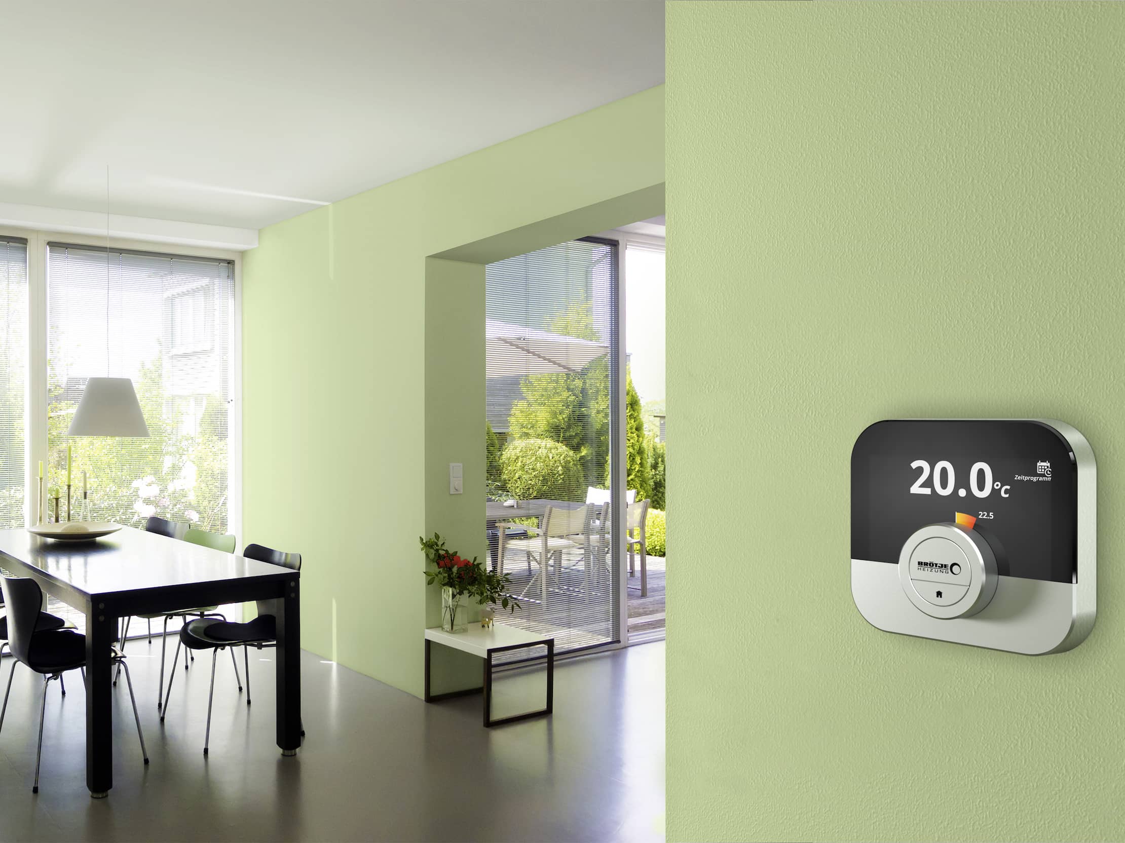 Die Regelung OT IDA ist ein einer hellgrünen Wand befestigt, dahinter sieht man das helle Esszimmer und Wohnzimmer mit Fenstern.