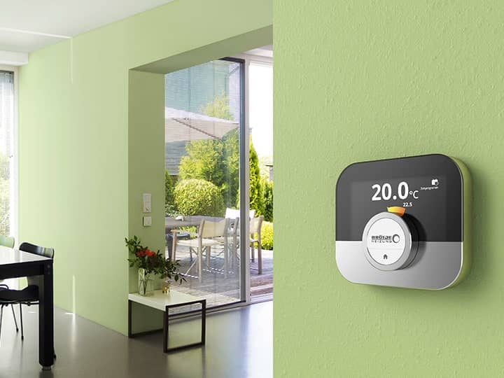 Die Regelung OT IDA ist ein einer hellgrünen Wand befestigt, dahinter sieht man das helle Esszimmer und Wohnzimmer mit Fenstern.
