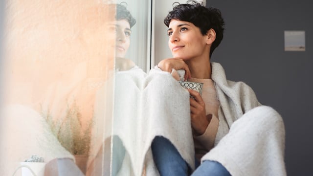 Frau sitzt am Fenster und genießt warme Temperatur in ihrem Zuhause