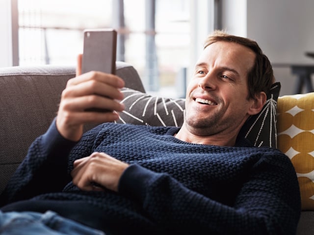 Mann liegt auf der Couch, schaut auf sein Handy und informiert sich online über Förderungen rund um Wärme