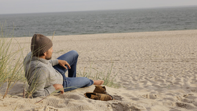 Mann liegt entspannt am Strand auf schaut aufs Meer