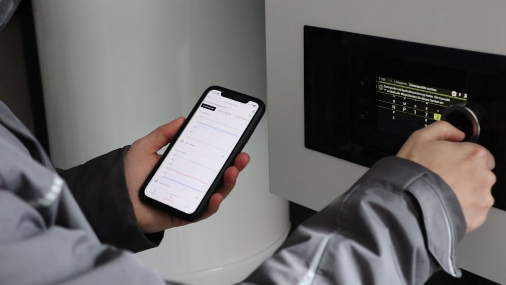 Handwerker schaut auf sein Handy und stellt eine Heizung ein