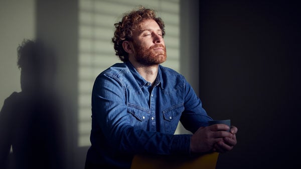 Mann sitzt vor einer Wand mit Sonne im Gesicht
