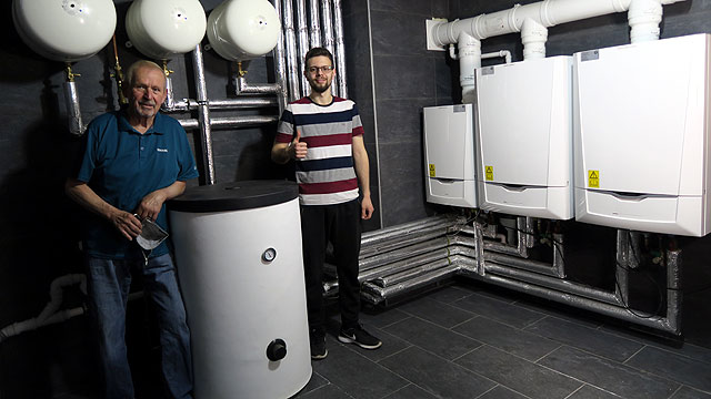 zwei Remeha-Mitarbeiter vor einem Gas-Brennwertkessel in einer Kaskade im Hintergrund.