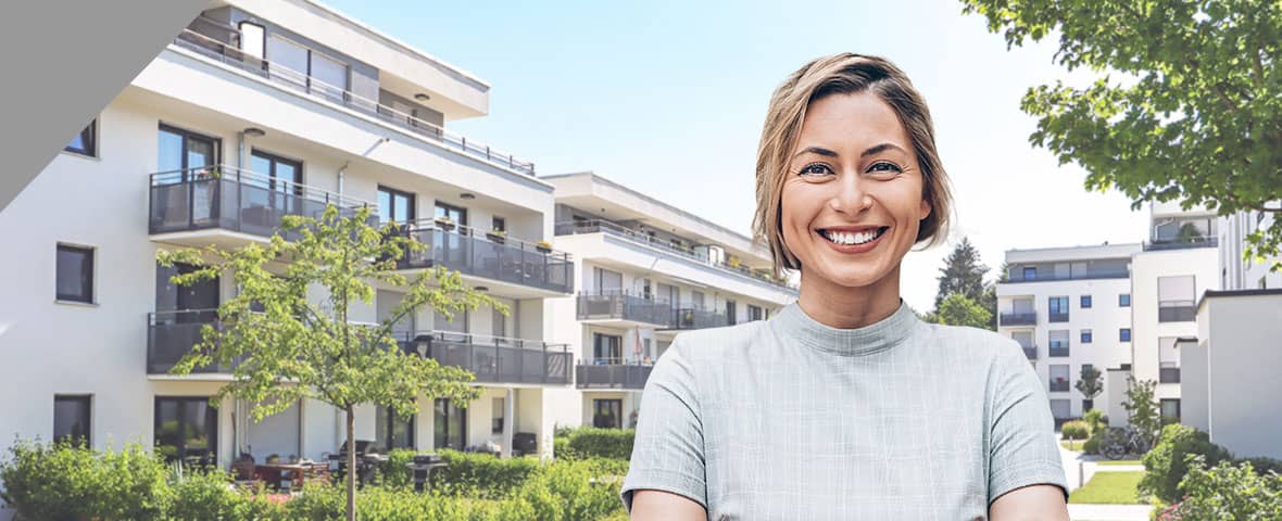 Lächelnde Frau vor einer Apartmentanlage mit Grünanlage
