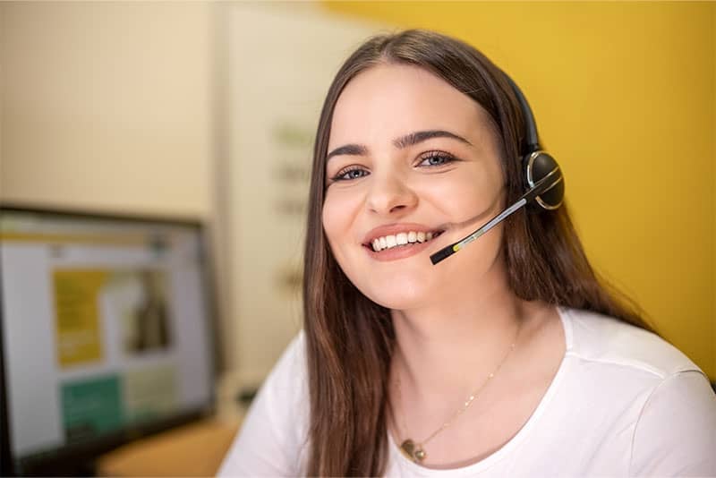 Junge Kollegin an der Remeha Zentrale mit Headset lächelt freundlich.