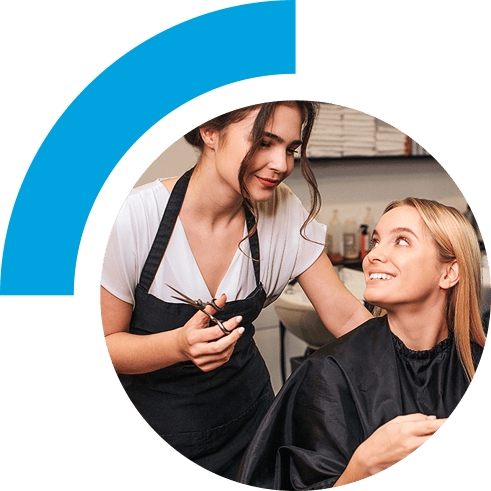 Hairstylist stands behind a smiling customer while holding phone