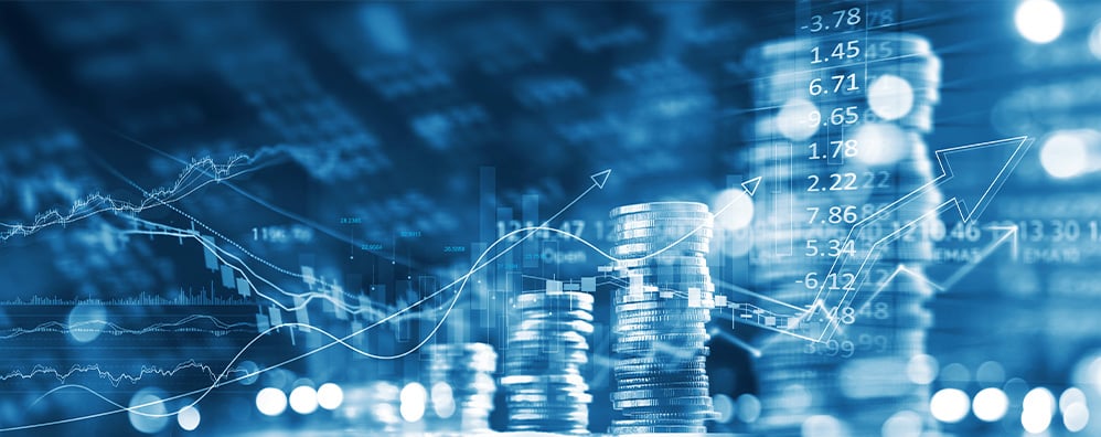 Alt text: Stacks of coins and upward-trending graphs on a blue-toned background, symbolizing financial growth and investment success.