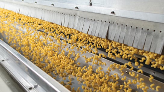 A conveyor belt with yellow pasta spirals being processed in a factory.