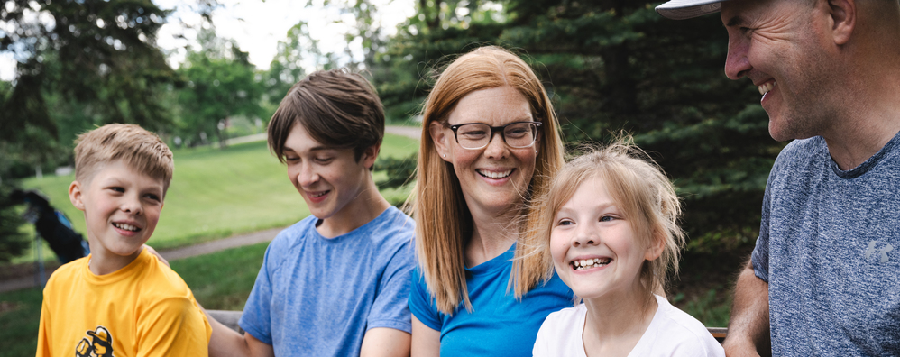 A family with mom, dad, two sons and one daughter sitting in a park filled with vibrant green grass and trees