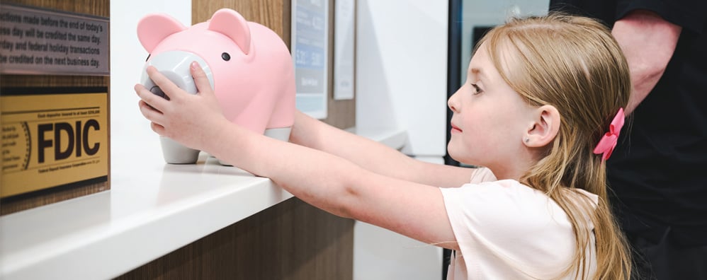 Child holding piggy bank at teller line