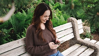 Woman sitting on a bench outside on their phone