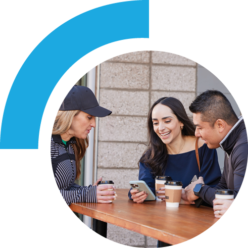 Three friends staring at the center person's phone while standing at a table with coffee cups.