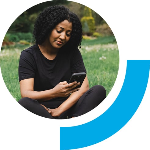 Woman on her phone while sitting in an open field of grass