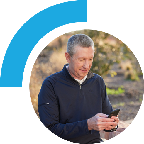 Middle-aged man using his phone. The background scenery is outdoor filled with brown and dark green plants.