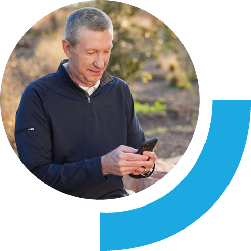 Middle-aged man using his phone. The background scenery is outdoor filled with brown and dark green plants.