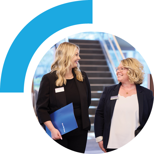 Two Bell employees walking and talking while one holds a folder. The setting is an office building.