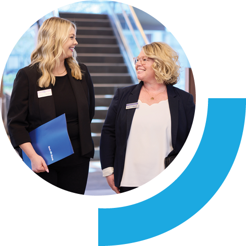 Two Bell employees walking and talking while one holds a folder. The setting is an office building.