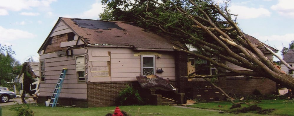 Large tree leaning on top of house after a storm.