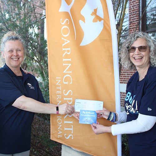 Jennifer and Soaring Spirits International rep holding a check in front of Soaring Spirits International banner