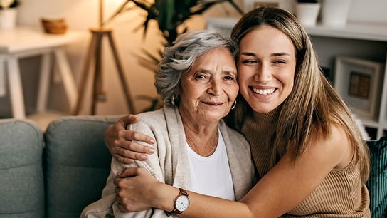 Young adult woman hugs an elder woman while sitting on a home couch