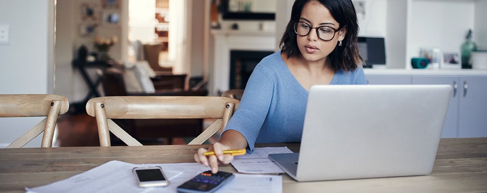 Woman scrolling through phone with laptop opened in her home