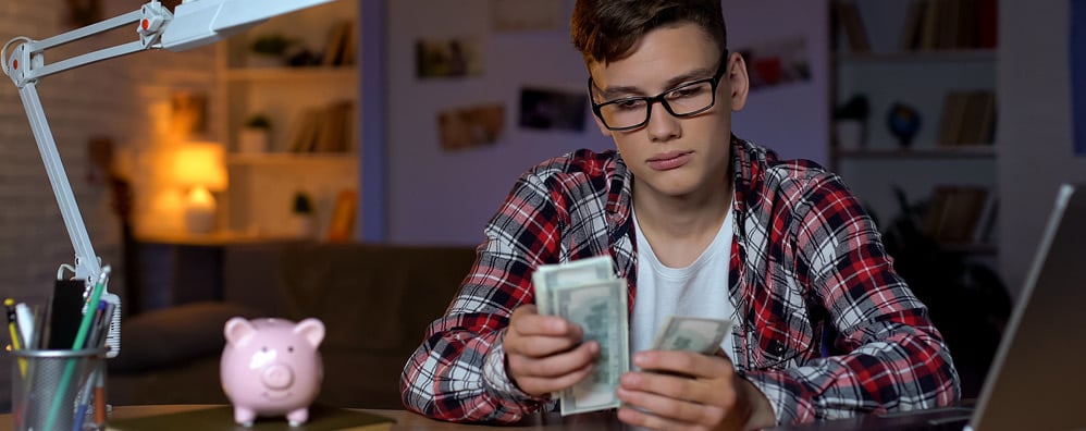 Kid sitting at desk with laptop open while counting money