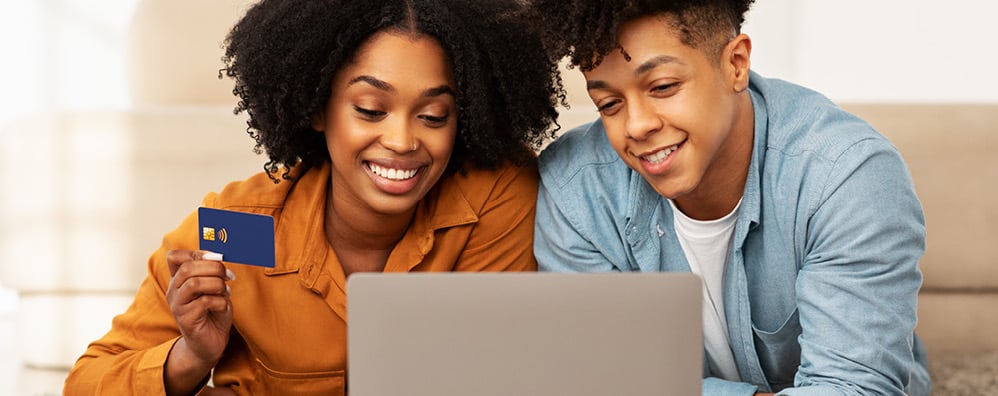 Mom and child looking at a laptop, mom is holding a debit card